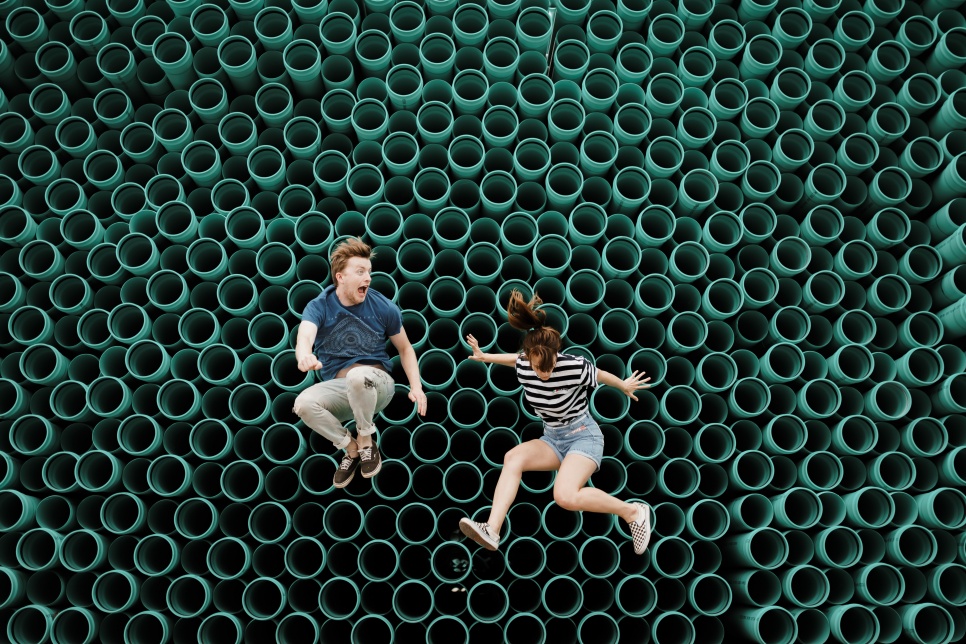 Two people jumping up in front of a tube wall
