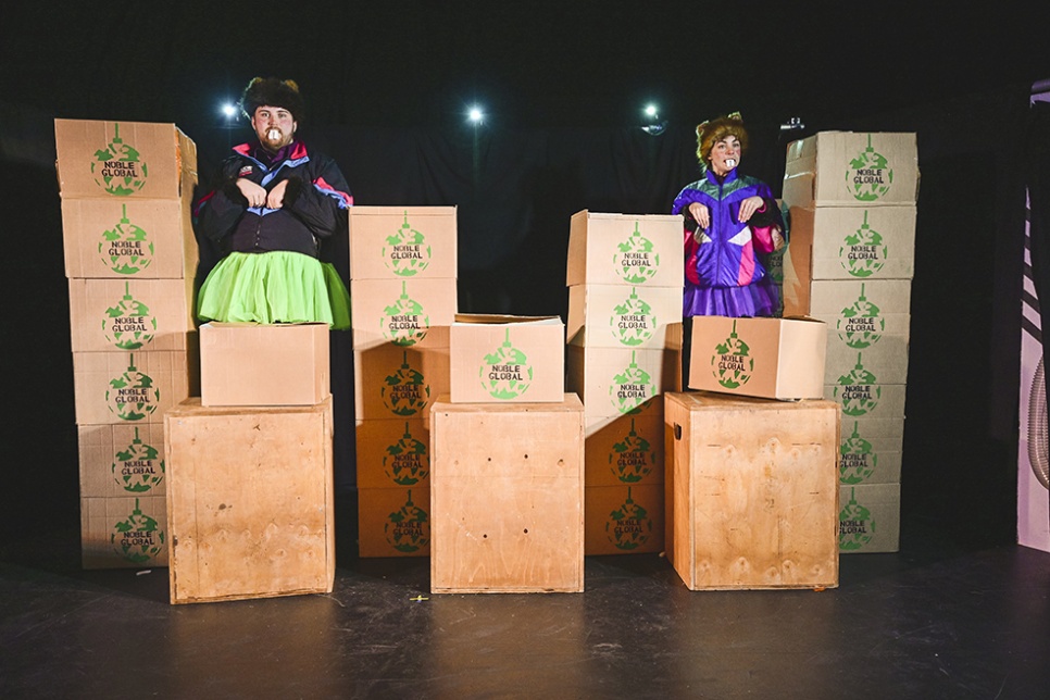 Two actors on a stage covered by boxes