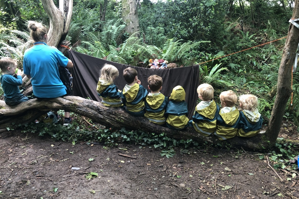 Thea de Klein, sat on a fallen tree with pupils from Aberporth Bilingual Playgroup