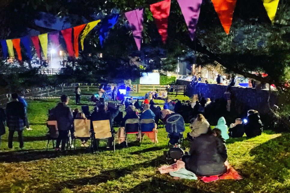 People sat outside on the grass watching a performance