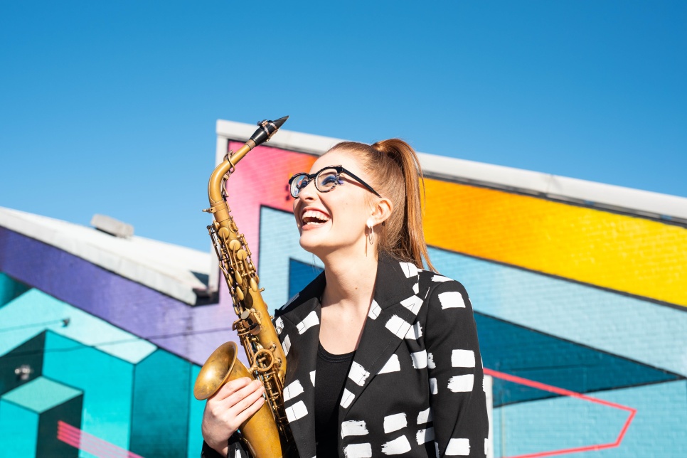 A person smiling holding a saxophone