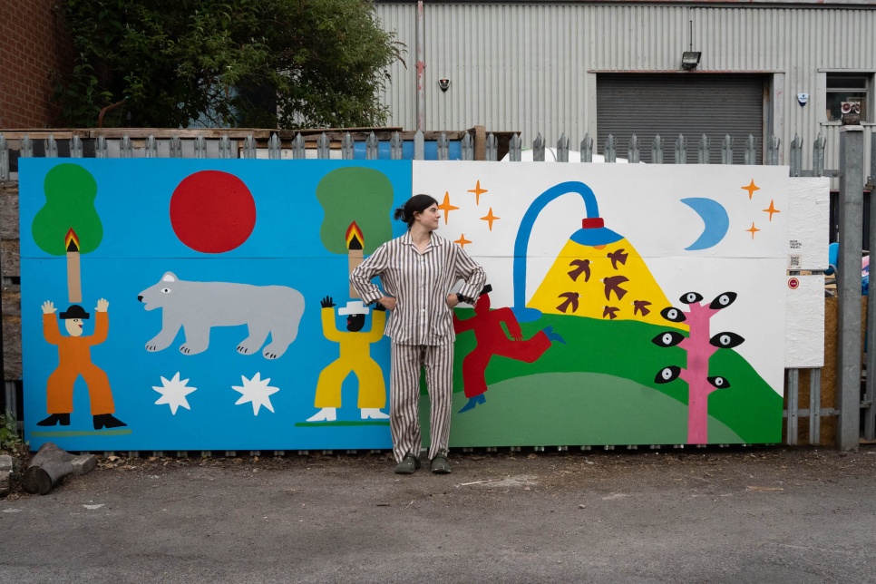 A photo of Artist Molly Sinclair-Thomson in front of the new brightly coloured PWSH mural at Spit & Sawdust