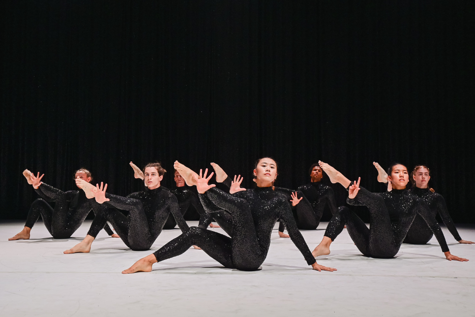 Dancers all dressed in black, all doing the same pose, sat on the floor