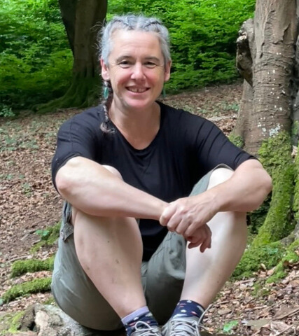 Fran Higginson sitting on a tree trunk in a forest, smiling at the camera.