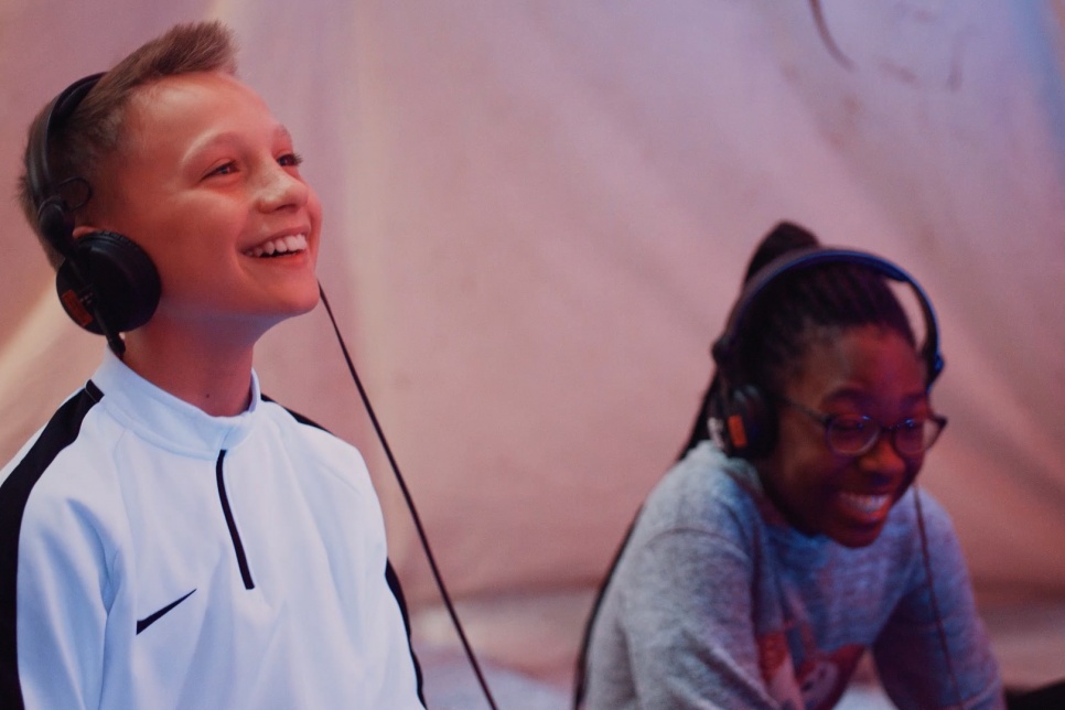 Two children wearing headphones and laughing