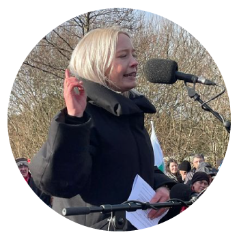 Mabli Siriol Jones outdoors speaking to a crowd with a microphone and wearing a black coat.