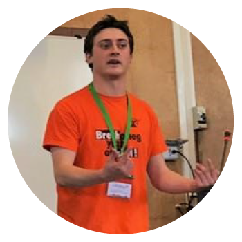 Talwyn Baudu wearing an orange t-shirt and lanyard in a teaching room.