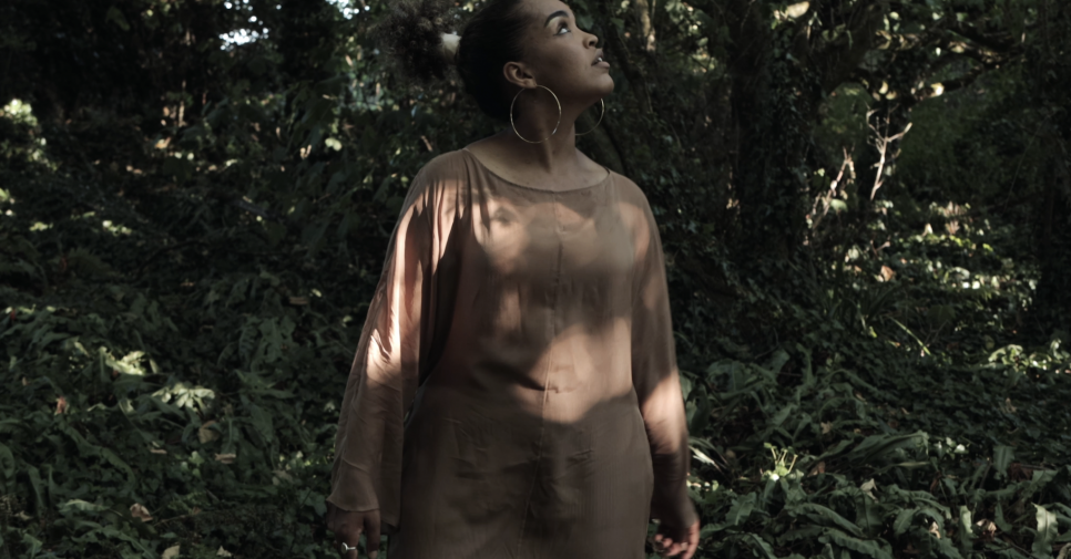 A woman in a brown dress looking up in a shady forest