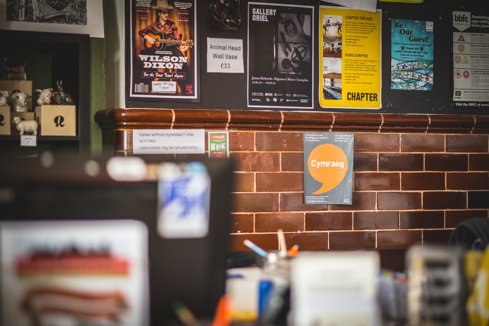 Posteri ar wal gyda poster Cymraeg yn y canol | POsters on a wall with the CYmraeg poster in the center