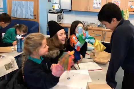 Four students playing with hand puppets in a classroom environment
