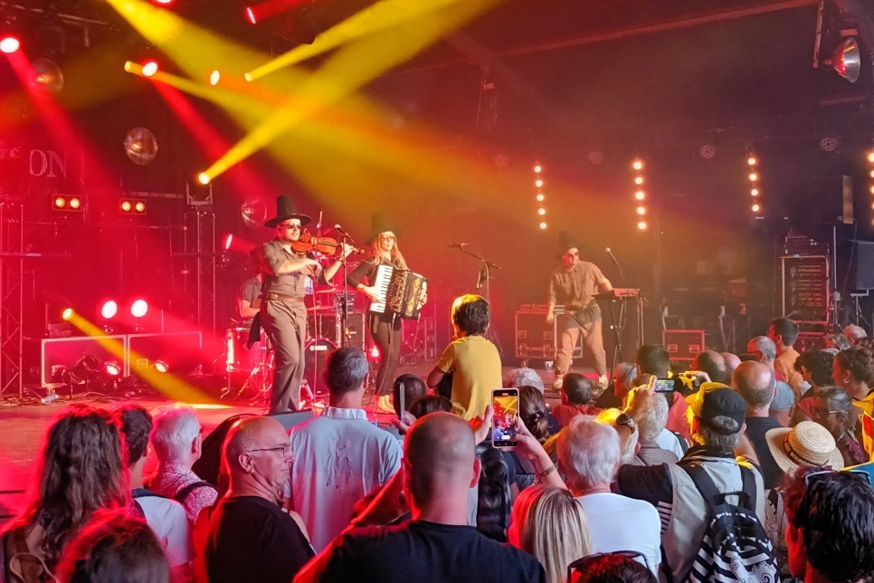 Band perform onstage with red and yellow lights, in front of a packed crowd.