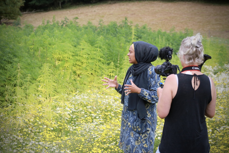 A videographer filming a person in front of green foliage