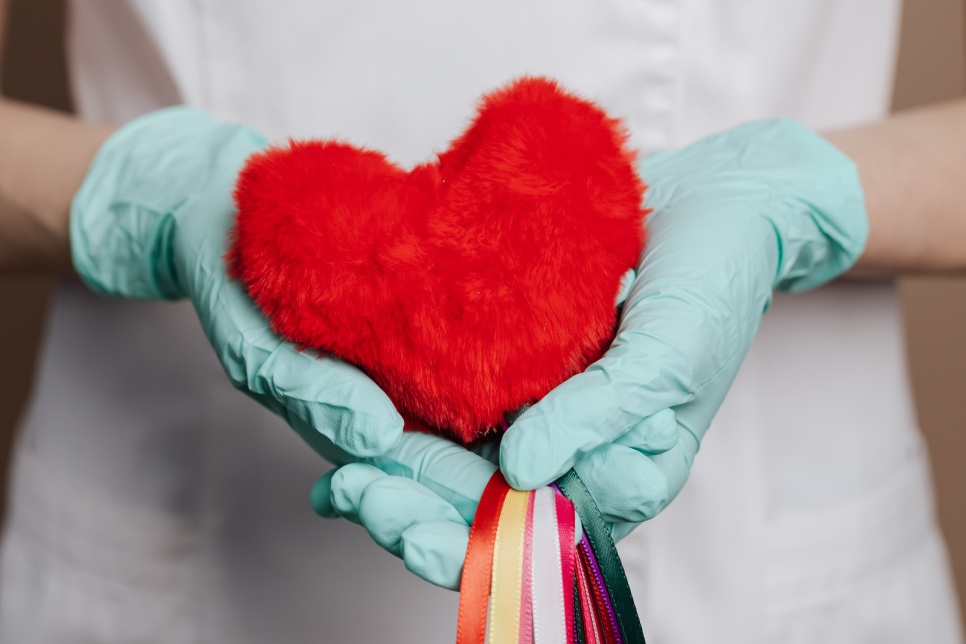 Person in white uniform holds out a red heart made using crafts and ribbons.