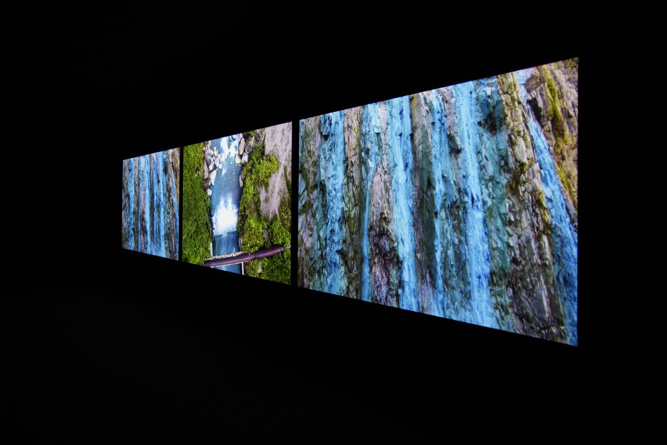 3 large screens of blue and green landscape photography, in a very dark room.