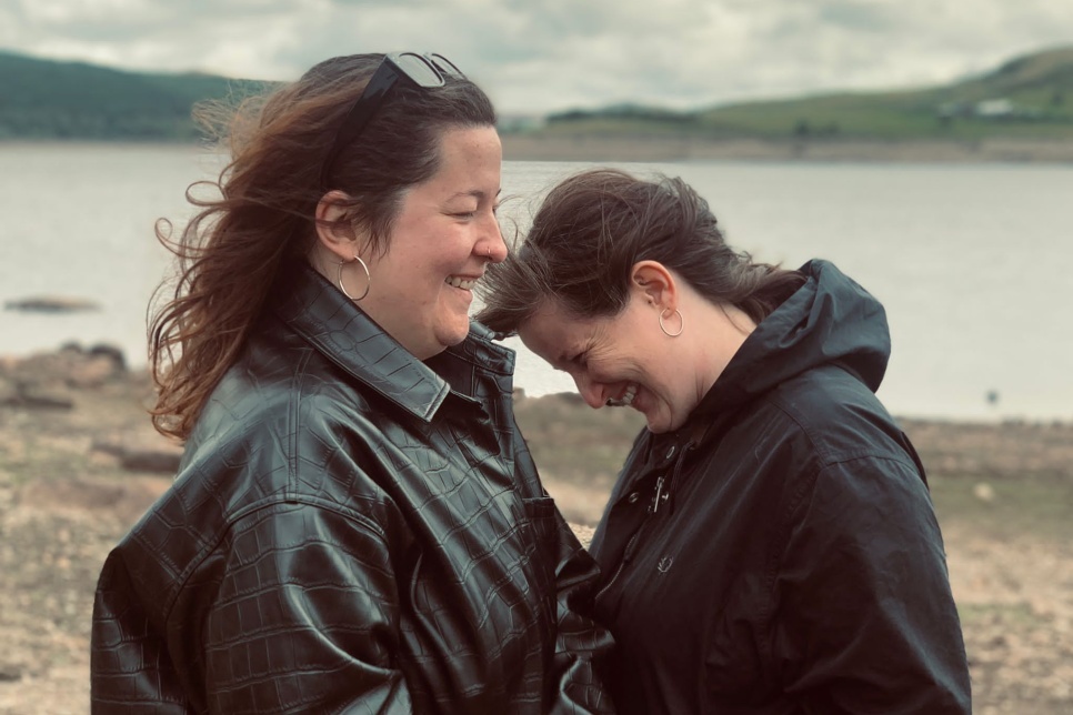 Artists Ffion Wyn Morris and Rhiannon White facing each other smiling in front of a Welsh lake