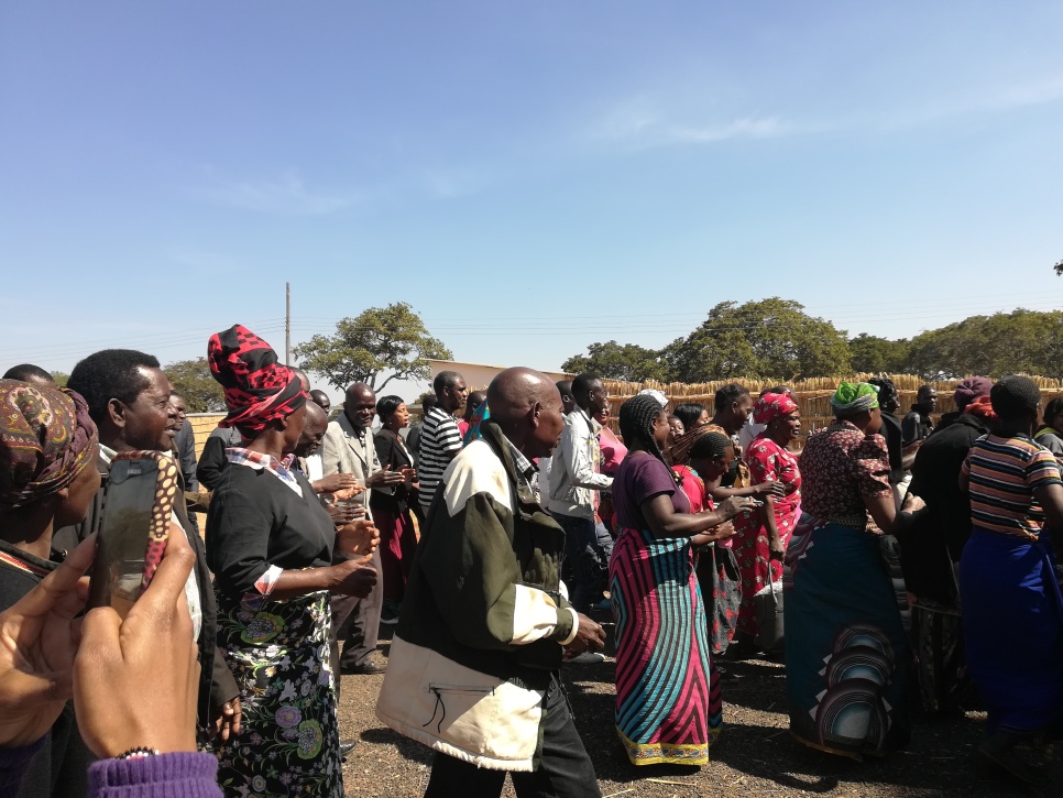 Group of people walking from left of screen to right of screen, some in traditional outfits 