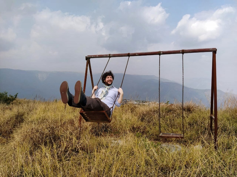 Gareth Bonello on a two seater swing in a field with blue and cloudy sky