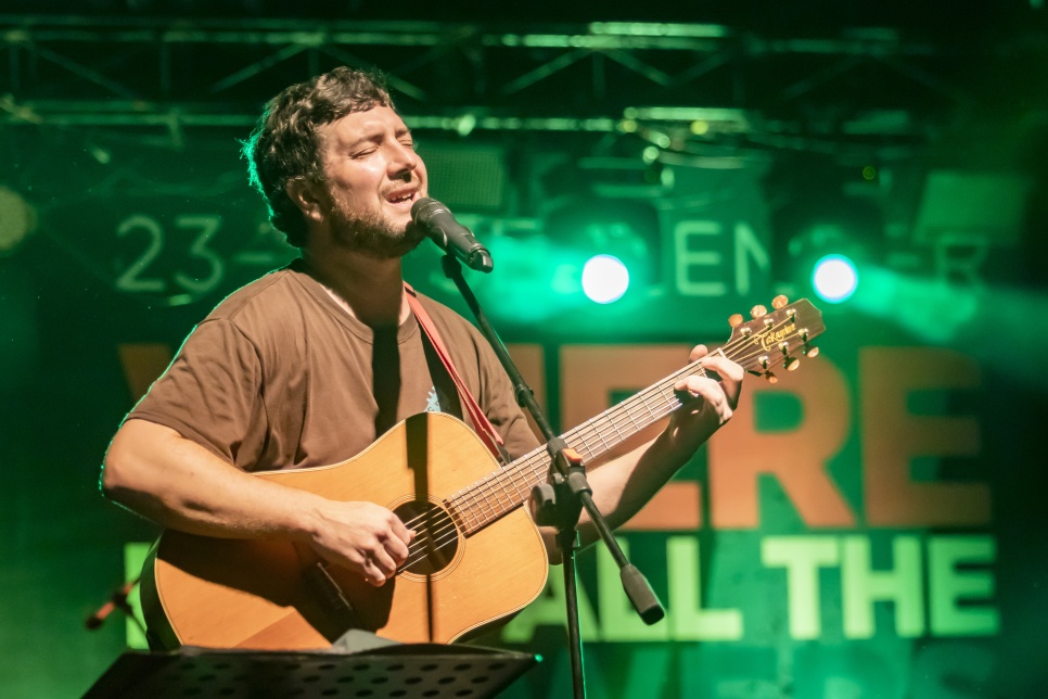 Gareth Bonello singing and playing a guitar on stage with a microphone on a stand 