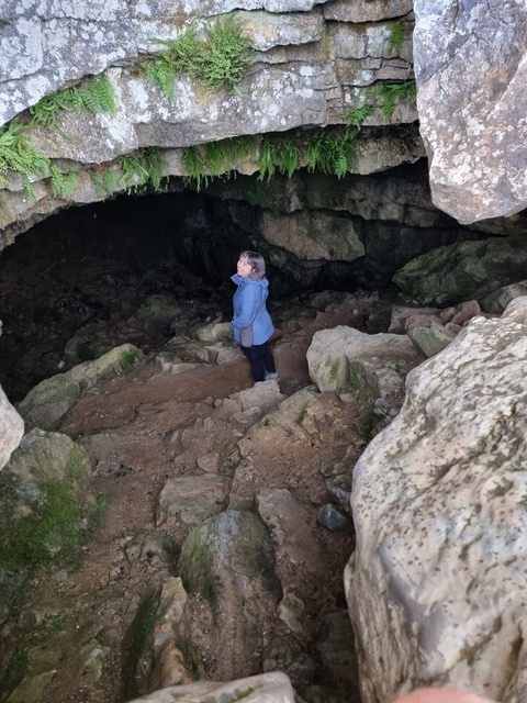 Georgina in the entrance to a rock cave wearing a blue rain coat 