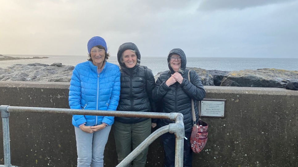 Three women stood by the sea in windy and wet weather
