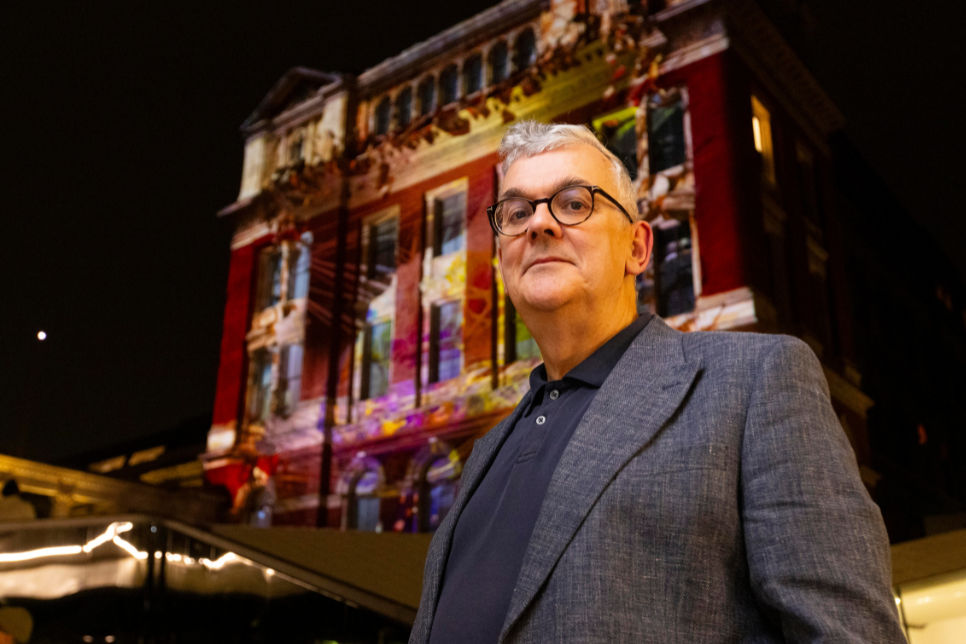 Berwyn Rowlands standing in front of a building with a colourful projected image at night