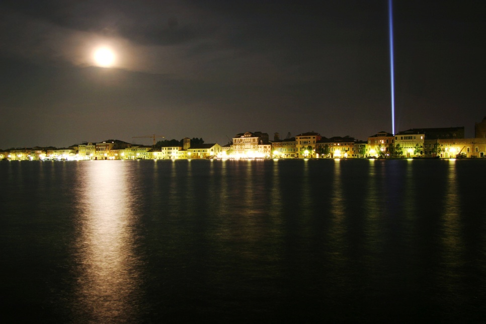 Venice by night with a blue light beam on the right hand side and the moon on the left