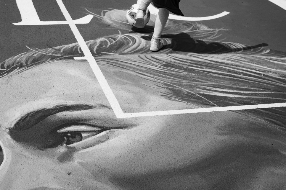 Close up of Jess Fishlock mural in black and white with child kicking a ball in the background