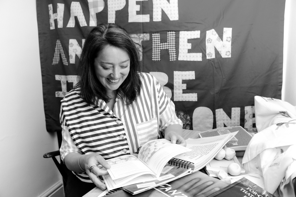 A woman in a striped shirt smiling at a book, in black and white