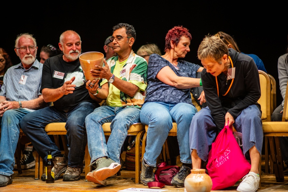Group of people sat on chairs, smiling and sharing pottery pieces