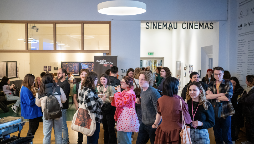 A crowd of people talking and smiling with the sign 'SINEMAU CINEMAS' in the background