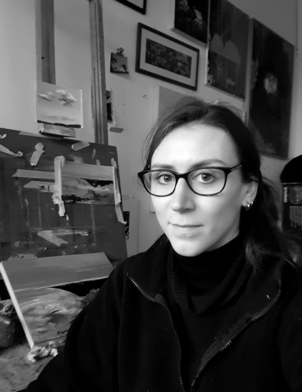A lady in glasses smiling in an art studio, in black and white.