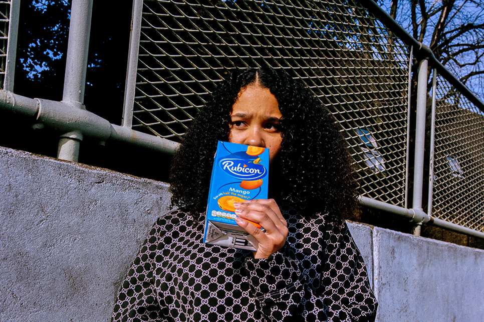 Photograph of a woman holding a mango juice carton in front of her mouth / Ffotograff o fenyw yn dal carton sudd mango o flaen ei cheg