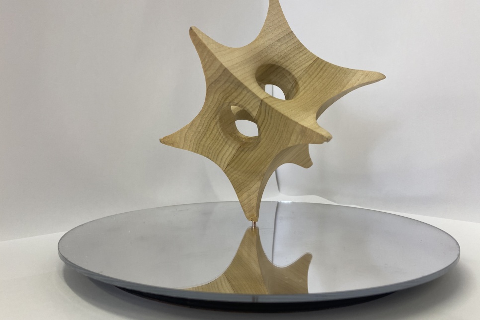 3D sculptural artwork suspended above a spherical mirrored disk on a white background / Gwaith celf cerfluniol 3D wedi'i gynnal uwchben disg sfferig drychog ar gefndir gwyn