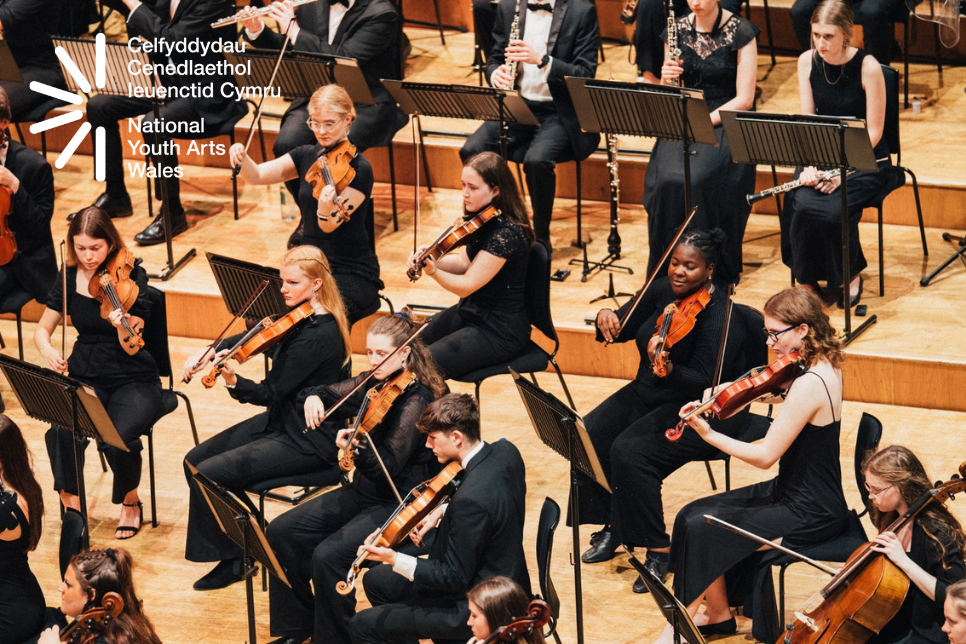Photograph of orchestra playing on stage / Ffotograff o gerddorfa yn chwarae ar lwyfan
