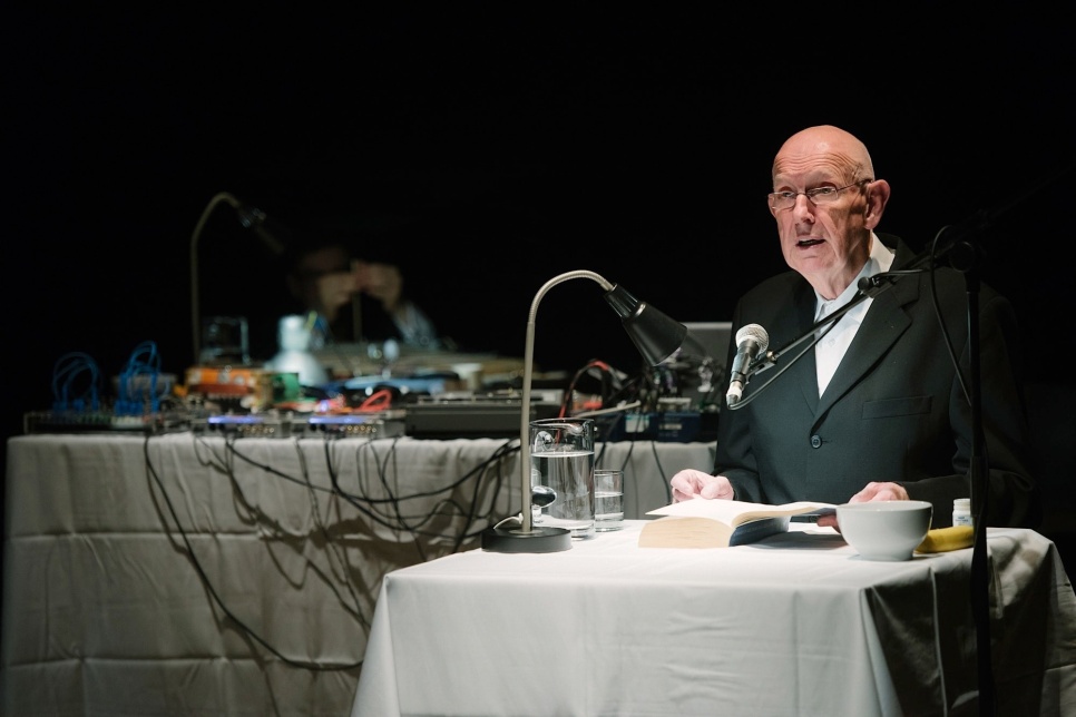 An image of a person speaking from the stage in front of a table