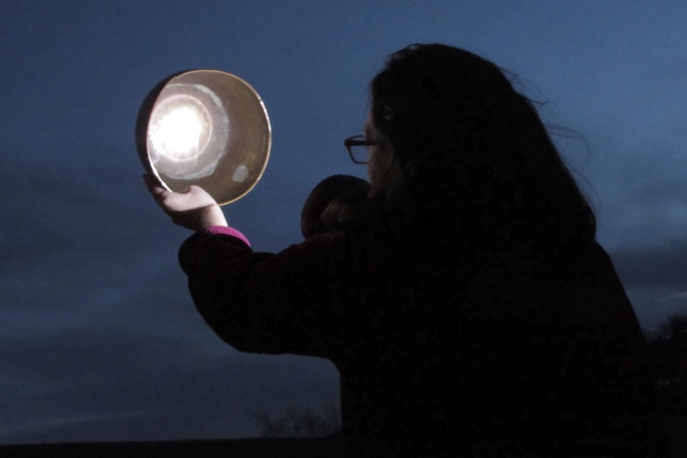A person holding a silver bowl up in the night sky