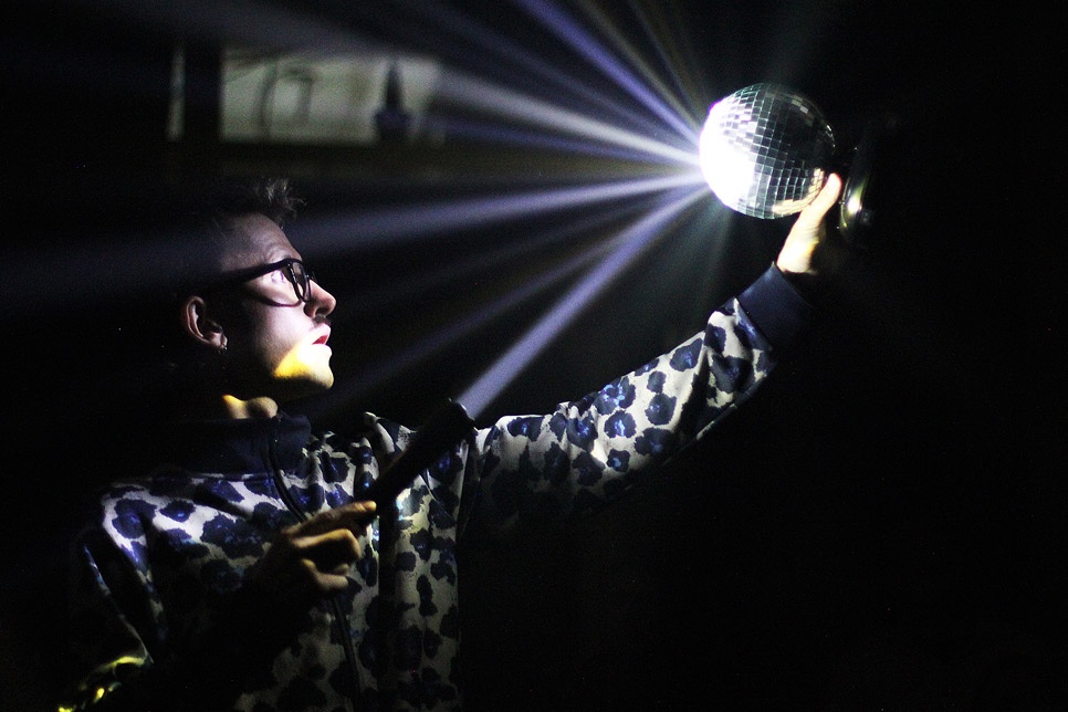 Photograph – a person in the dark lighting a small disco ball with the light of a torch / Ffotograff – person yn y tywyllwch yn goleuo pêl ddisgo fach gyda golau tortsh