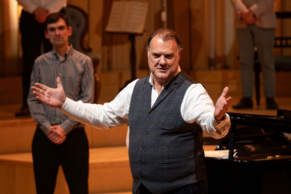 Photograph - Sir Bryn Terfel stands on stage with his arms open wide smiling / Ffotograff - Syr Bryn Terfel yn sefyll ar lwyfan gyda'i freichiau ar led ac yn gwenu