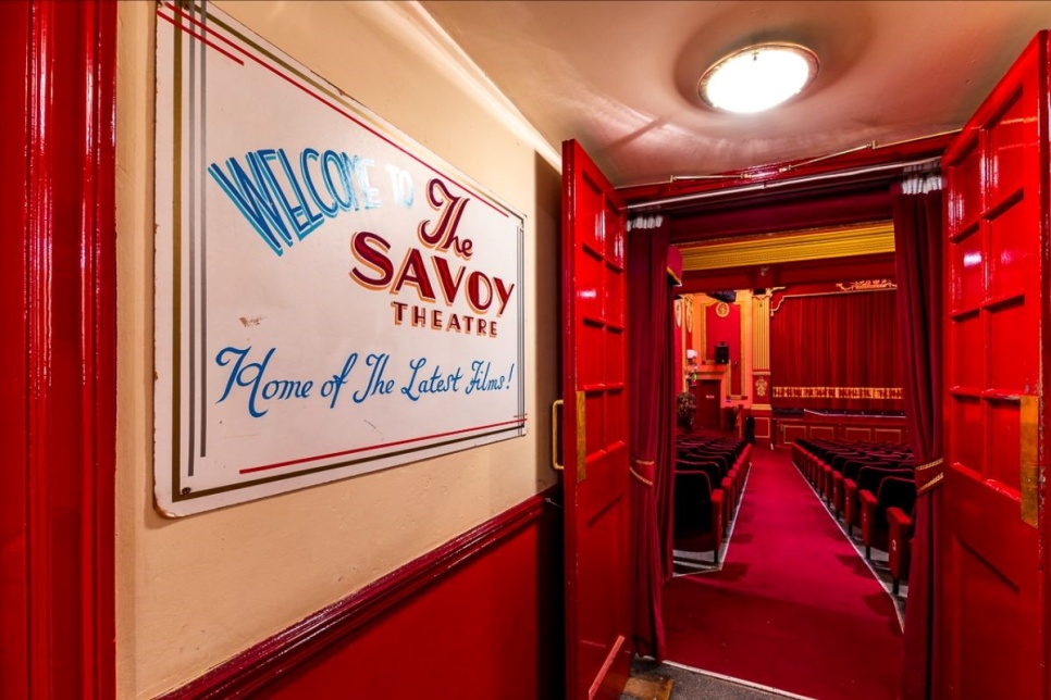 An image of The Savoy Cinema, which has red seats and a red auditorium. On the wall it reads 'The Savoy'