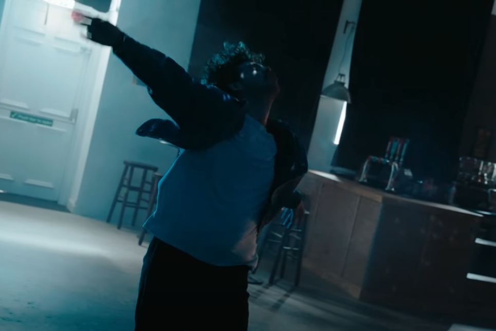 Photograph - A person in a room with arms held up high behind them as if in dance / Ffotograff - Person mewn ystafell yn dal eu breichiau yn uchel y tu ôl iddyn nhw fel petasent yn dawnsio