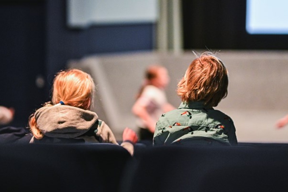 Two children sat down watching other children perform