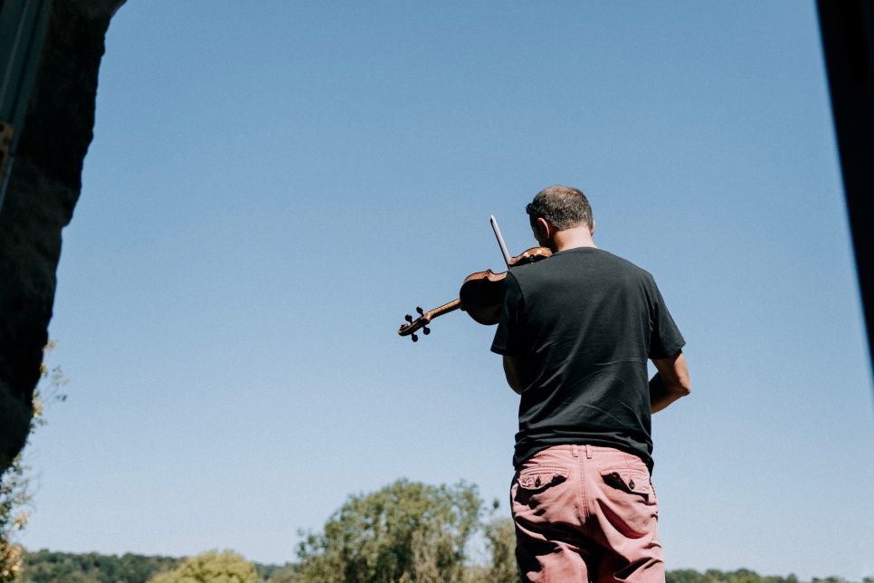 Man playing a fiddle with his back to the photographer - against a blue sky